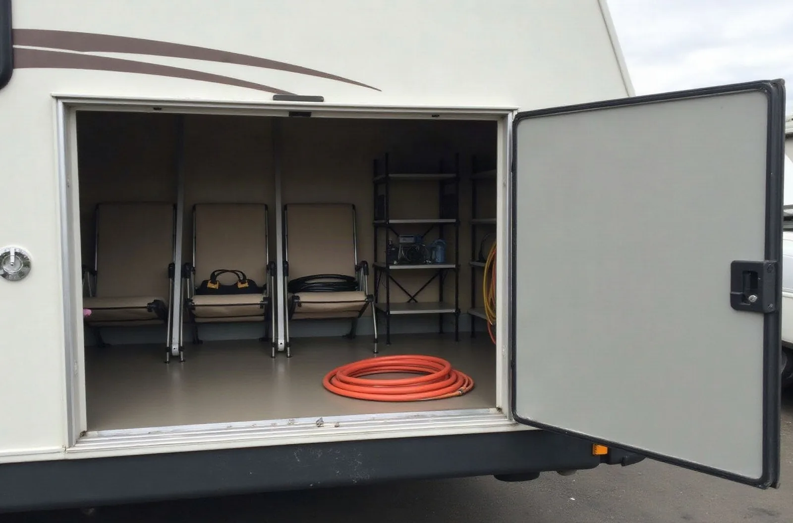Enclosed storage room attached to a metal carport, door open, shelves with lawn chairs and hoses, RV carport with storage.