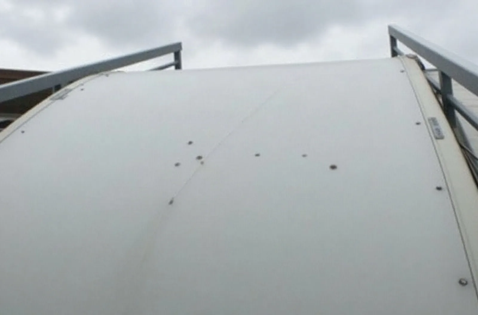 Small hail dents on a fifth wheel RV roof seen from a ladder under an overcast sky, a common claim covered by RV storage insurance.