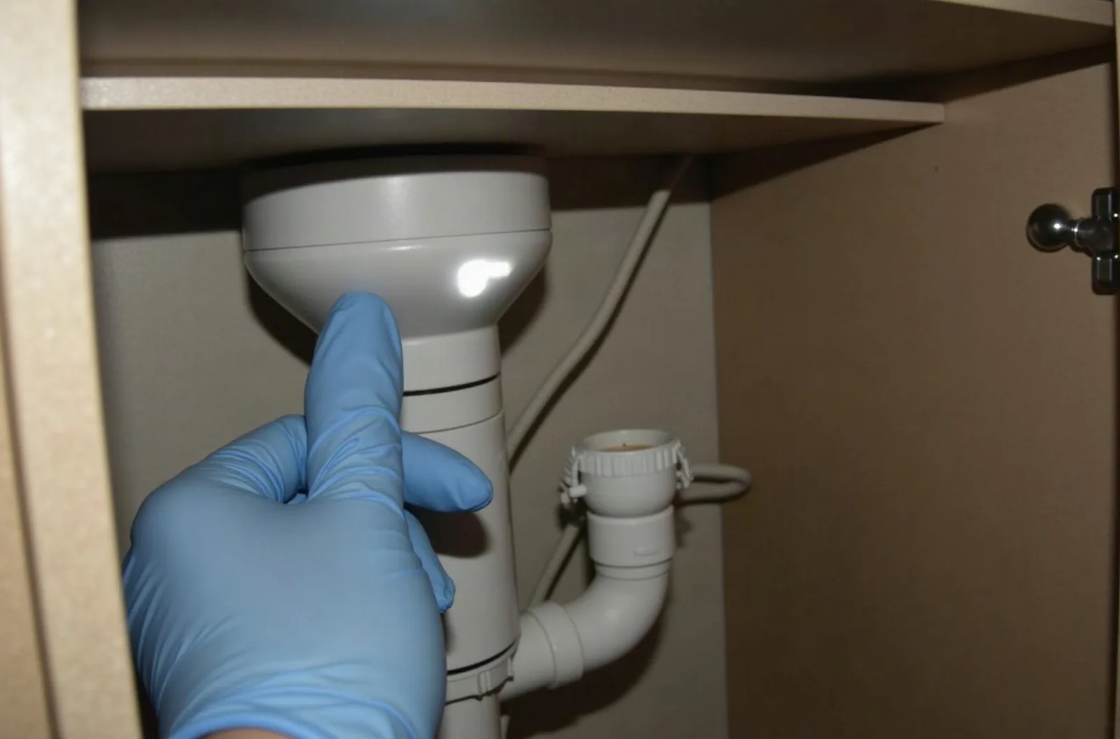 Gloved hand setting a snap trap near plumbing inside an RV cabinet with a flashlight beam, demonstrating RV storage tips for pest prevention.
